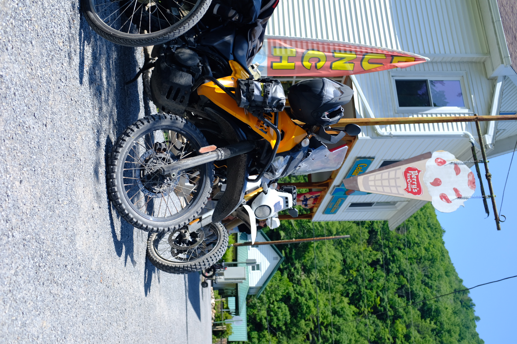 Dual-sport bikes parked outside a small-town general store with a lunch flag