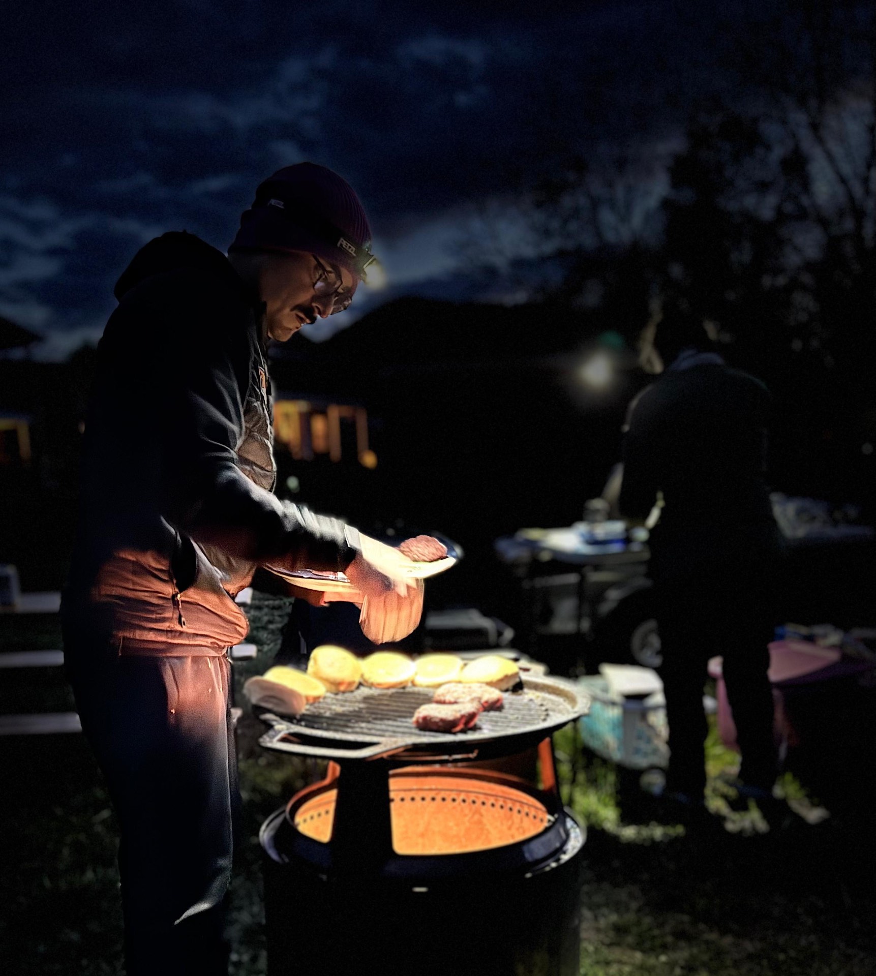 Anthony grilling burgers and toasting buns at camp after dark
