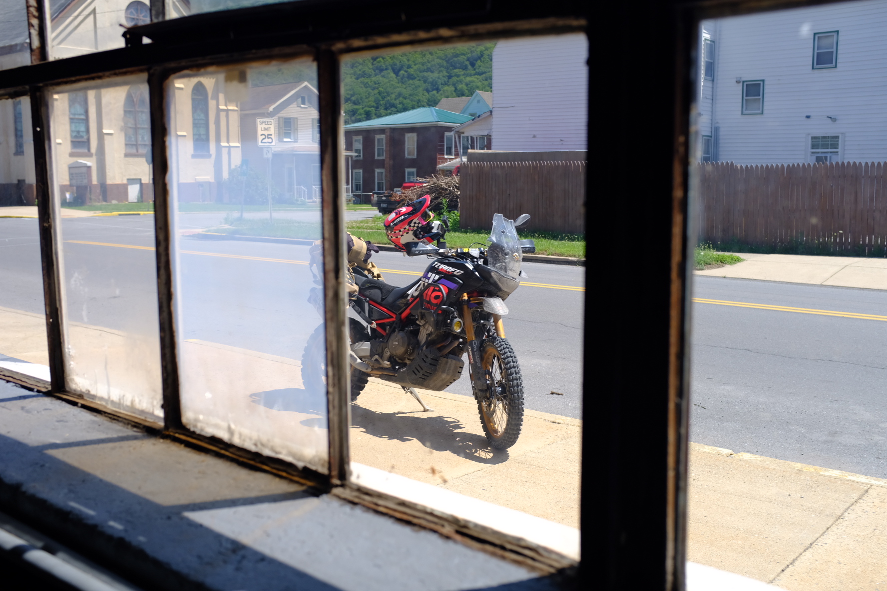 Adventure bike parked on a small-town street seen through a diner window