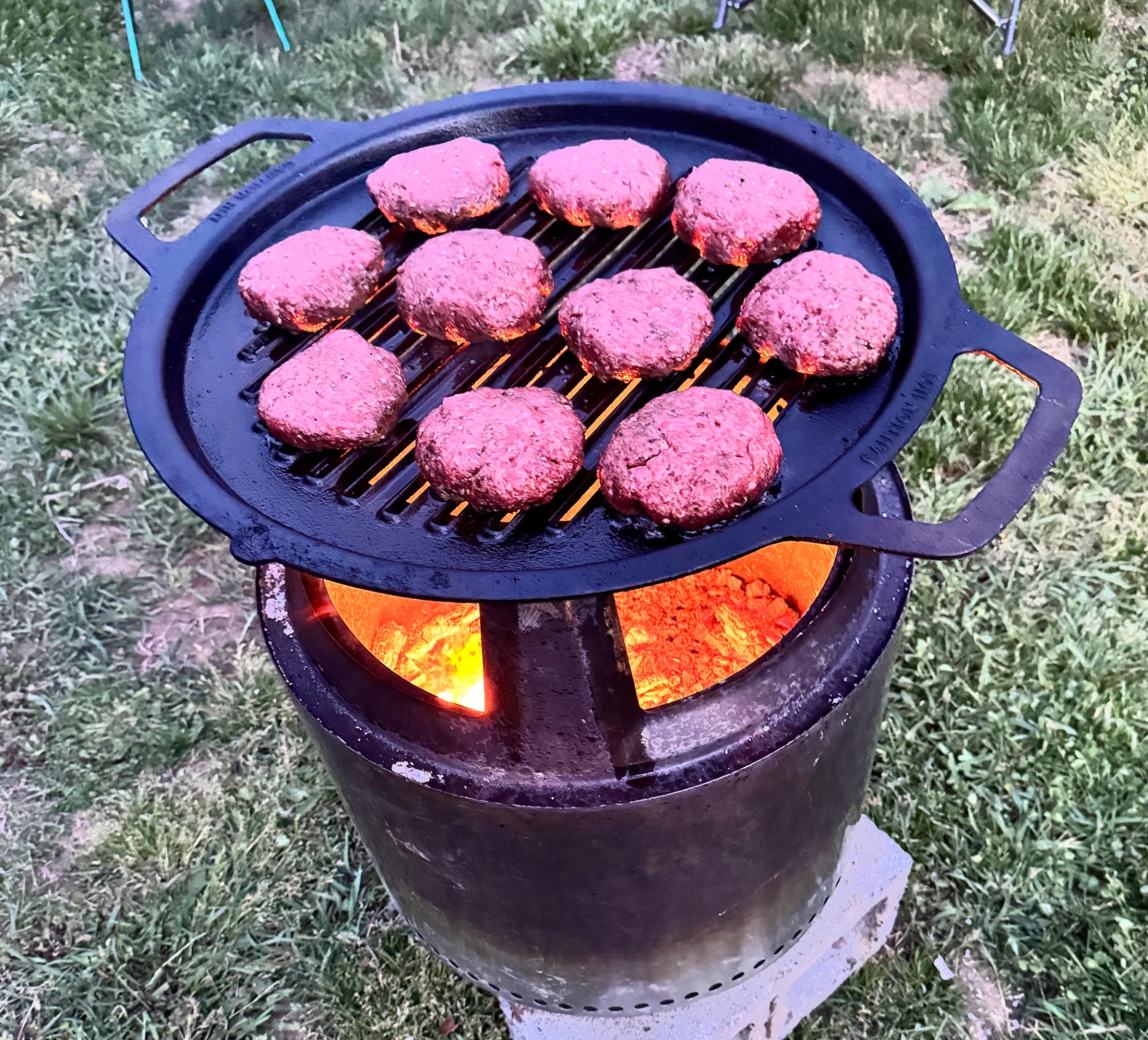 Burgers cooking over the fire on a cast iron grill
